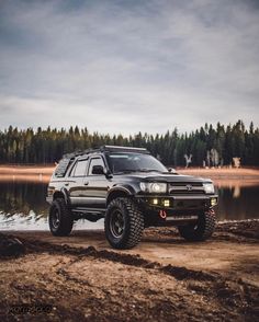 a black suv parked on top of a dirt field next to a body of water