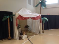 a white tent sitting on top of a floor next to black curtains and palm trees