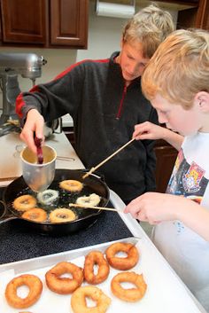 two young boys making donuts in a kitchen with one boy stirring them into a frying pan