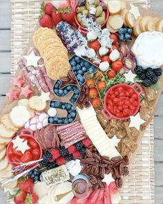 a platter filled with cheese, crackers, fruit and other food on top of a wicker mat