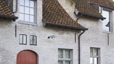 two red doors are on the side of a white brick building with brown shingles