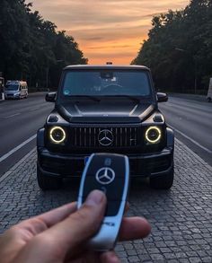 a hand holding a remote control in front of a black mercedes benz truck at sunset