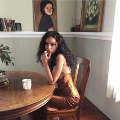 a woman sitting at a wooden table with a coffee cup in front of her face