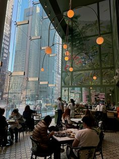 people are sitting at tables in the middle of a large room with glass walls and floor to ceiling windows