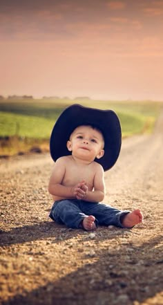 a baby wearing a cowboy hat sitting on the side of a road