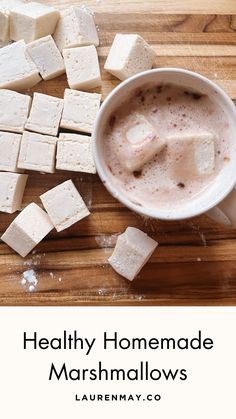 marshmallows on a wooden cutting board next to a cup of hot chocolate