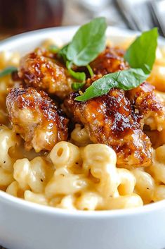 a white bowl filled with macaroni and cheese covered in chicken wings, garnished with green leaves