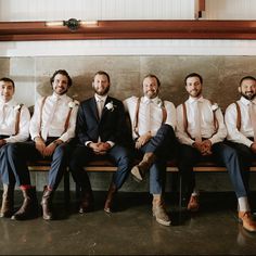 a group of men sitting next to each other on top of a wooden bench in front of a wall