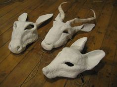 three white masks are sitting on the floor next to each other, one is wearing a cow's head