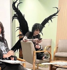 two women sitting in chairs with black wings on their backs and one holding a cell phone