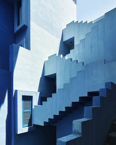 blue stairs leading up to a building with windows and shutters on each side, in front of a white wall