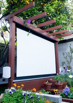 an outdoor movie screen surrounded by potted plants