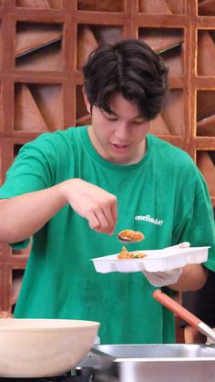 a young man in a green shirt is eating food from a paper plate on top of a stove