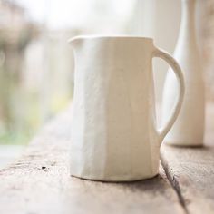 two white vases sitting on top of a wooden table next to eachother