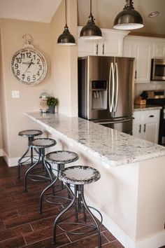 a kitchen counter with four stools in front of it and a clock on the wall