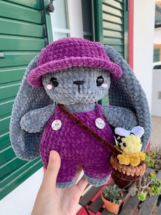 a hand holding a small stuffed animal in a purple outfit