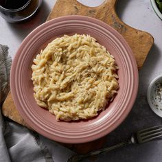 a pink plate topped with macaroni and cheese on top of a wooden cutting board