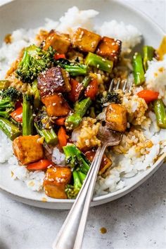 a plate with rice, broccoli and tofu on it next to a fork