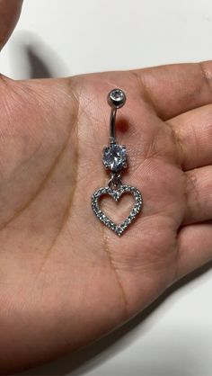 a person holding a heart shaped belly ring in their left hand, with a diamond dangling from it