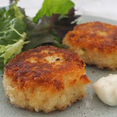 two crab cakes on a plate with lettuce and mayonnaise next to it