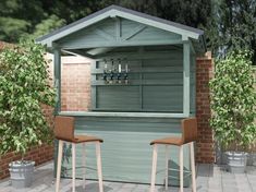 two wooden stools sitting in front of a small green building with barstools