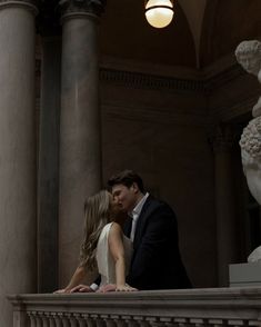 a bride and groom kissing on the balcony of a building with statues in the background