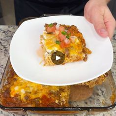 a person holding a white plate with food on it in front of a casserole dish