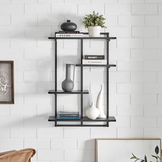 a shelf with vases, books and other items on it in front of a white brick wall