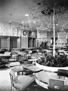 an old black and white photo of a restaurant with tables, chairs, and plants