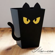 a black paper bag with yellow eyes and a cat's head on it, sitting on a wooden table