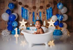 a baby sitting in a bathtub surrounded by blue and white balloons, stars and streamers