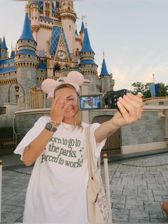 a woman taking a selfie in front of the castle at disney world with her cell phone