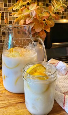 two glasses filled with lemonade sit on a table next to a pitcher and towel