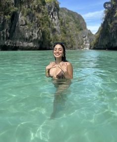 a woman is floating in the water near some rocks and cliffs, with her hands on her chest