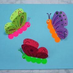 three paper butterflies on a blue background with one green, one pink and one orange