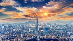 an aerial view of a city with skyscrapers and mountains in the background at sunset