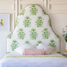 a white bed with green and pink wallpaper next to a vase filled with flowers