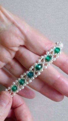 a woman's hand holding a green and white bracelet with pearls, beads and emeralds