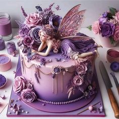 there is a cake decorated with purple flowers and a fairy on the top, surrounded by cupcakes