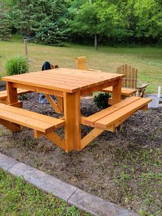 a wooden picnic table sitting in the middle of a field next to a park bench