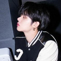 a young man with black hair wearing a varsity jacket and earring sitting in front of a computer