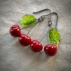 four cherries with green leaves hang from silver earwires on a white surface