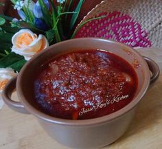 a bowl filled with sauce sitting on top of a wooden table next to some flowers