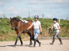 two people are walking their horses in the dirt