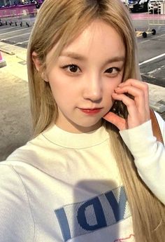 a girl with long blonde hair is talking on her cell phone while standing in an empty parking lot