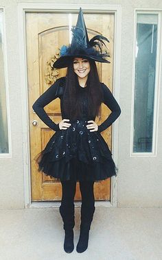 a woman wearing a witch costume standing in front of a door with her hands on her hips