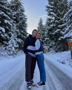 a man and woman hugging on the side of a road in front of snow covered trees