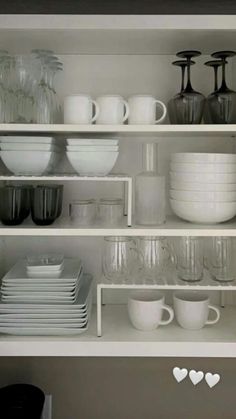 white dishes and cups are stacked on the shelves in this kitchen, which is organized with glassware