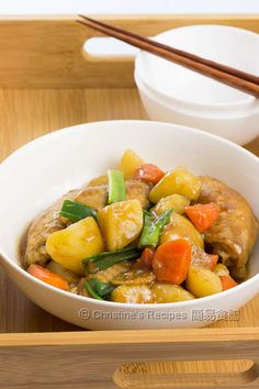 a white bowl filled with meat and veggies next to chopsticks on a wooden tray