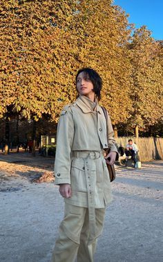 a woman standing in front of a tree wearing a trench coat and holding a purse